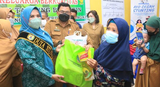Ketua TP PKK Sergai Ny. Hj. Rosmaida Saragih Darma Wijaya (kiri),memberikan bantuan sembako saat membuka kegiatan Penguatan Kampung KB dan Percepatan Penurunan Stunting bertempat di Aula Kantor Desa Pekan Tanjung Beringin Selasa (19/4/2022).  